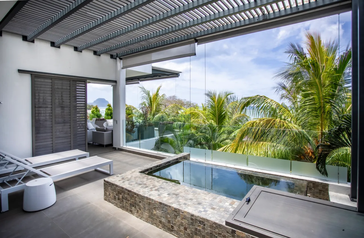 Espace extérieur avec piscine et chaises longues, entouré de verdure. Éclairage naturel abondant.