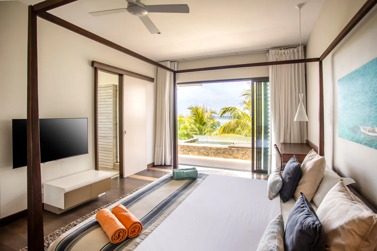 Chambre lumineuse avec un lit à baldaquin et accès direct à la terrasse. Vue sur la végétation et la piscine.