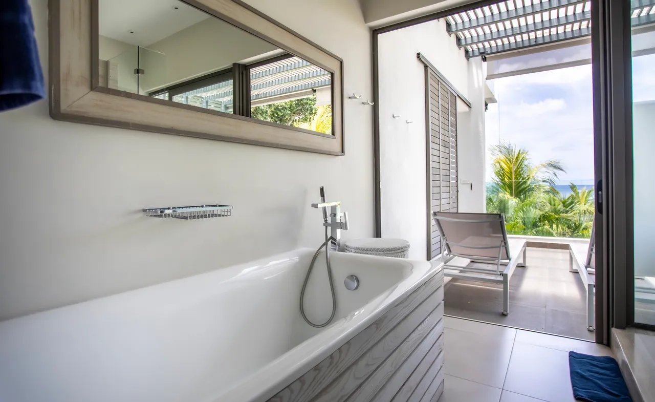 Salle de bain avec baignoire encastrée et accès à un balcon privé. Miroir et éclairage naturel.
