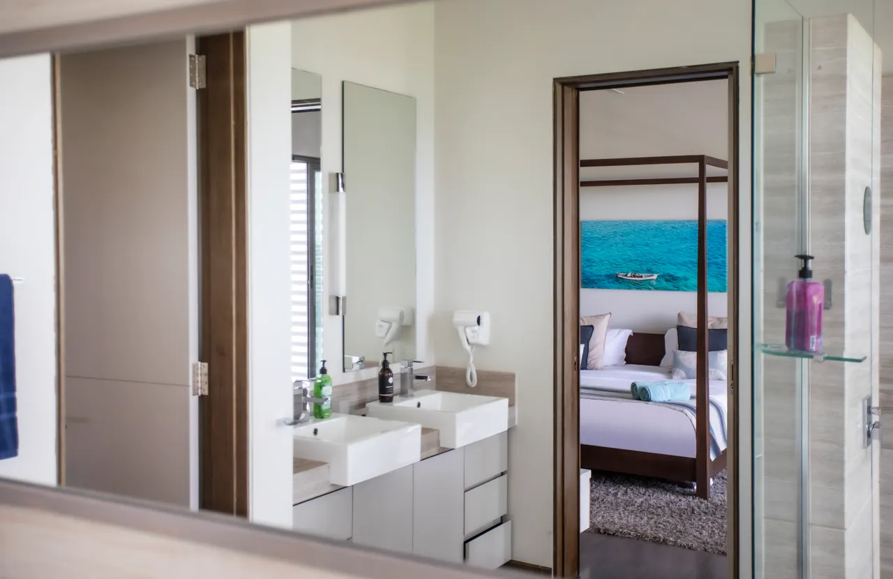 Salle de bain avec deux lavabos et espace de rangement. Miroir réfléchissant et éclairage moderne.