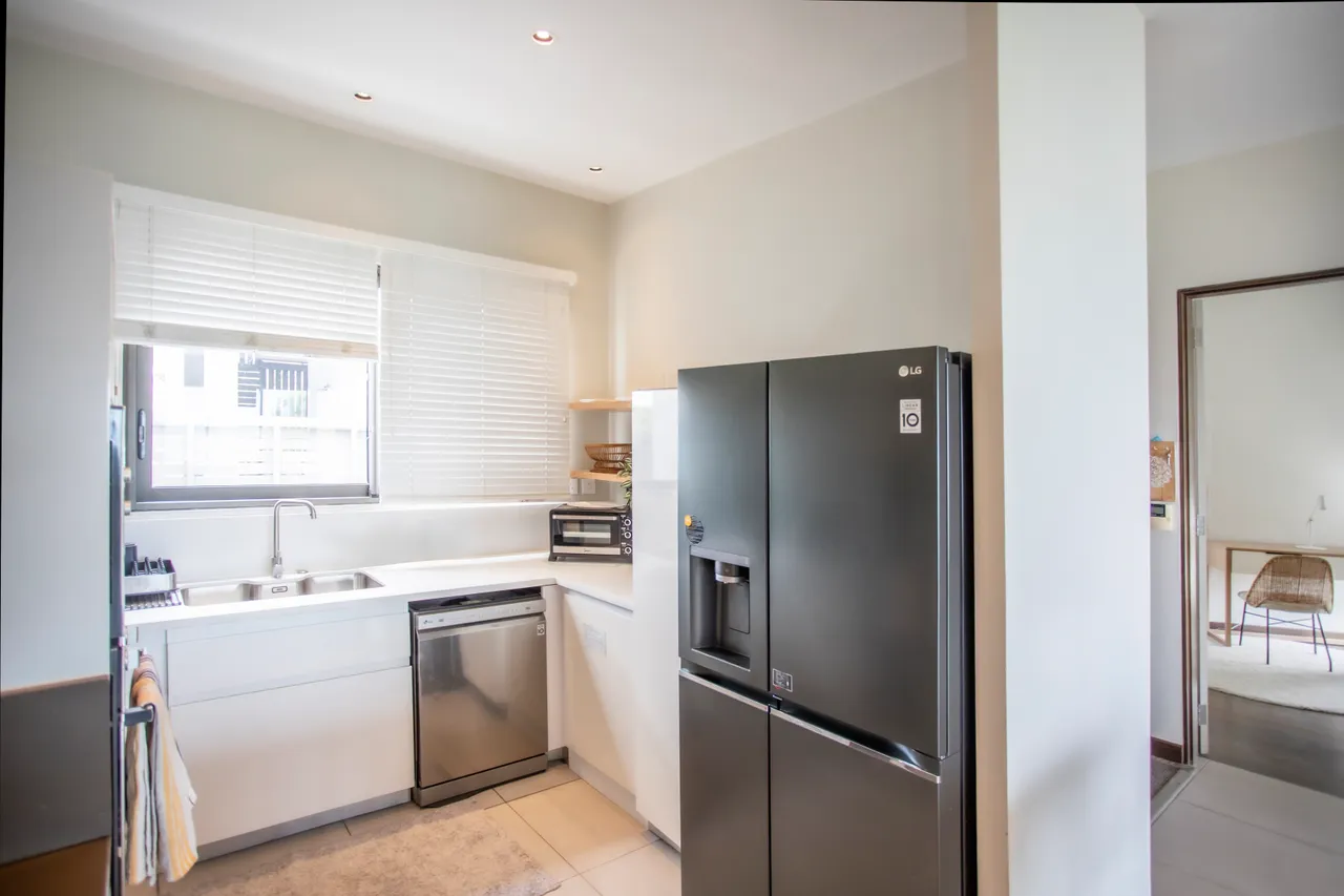 Cuisine minimaliste avec électroménagers intégrés et fenêtres à persiennes. Éclairage fonctionnel et surfaces blanches.