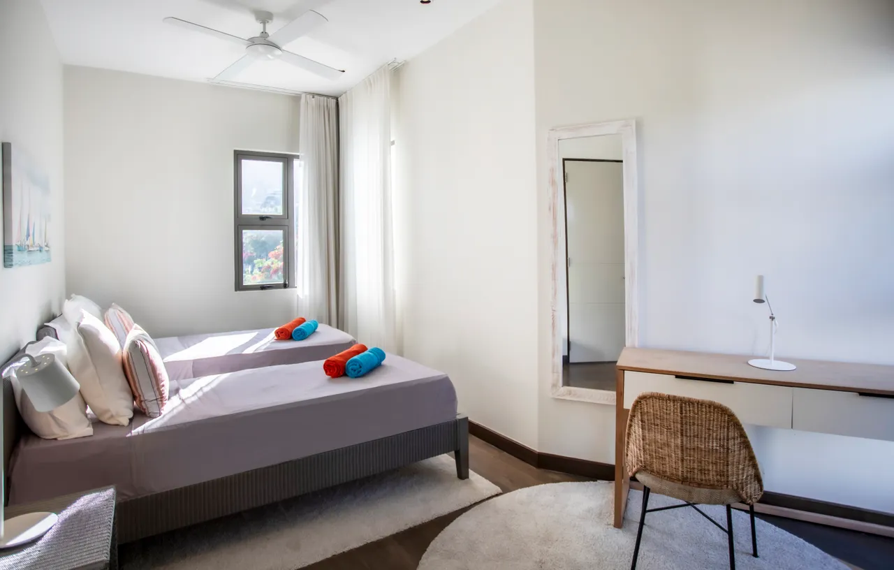 Chambre avec deux lits simples et bureau en bois. Éclairage naturel et textile coloré.