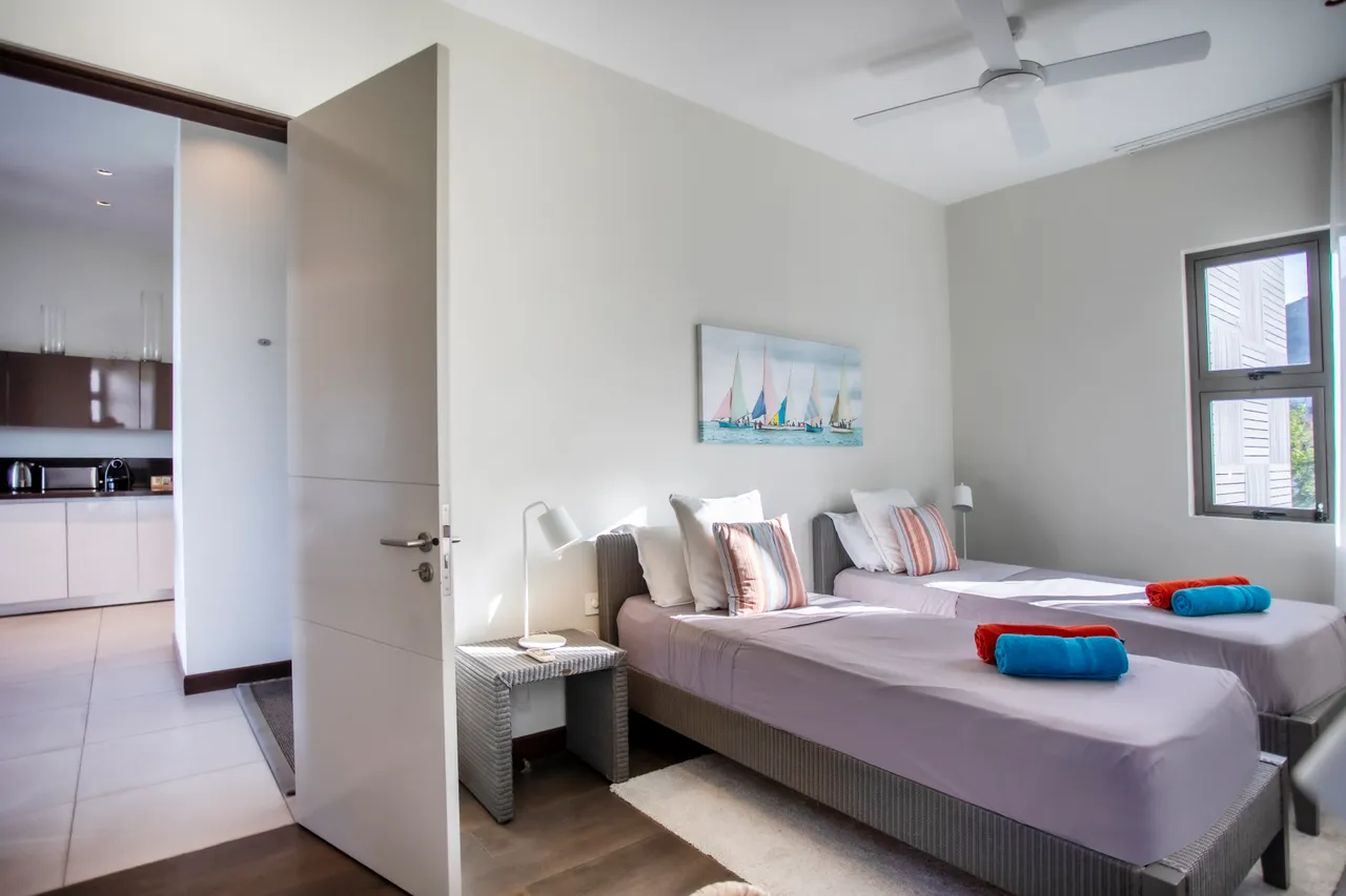 Chambre avec deux lits simples, fenêtres offrant une vue sur l'extérieur. Éclairage naturel et décoration sobre.