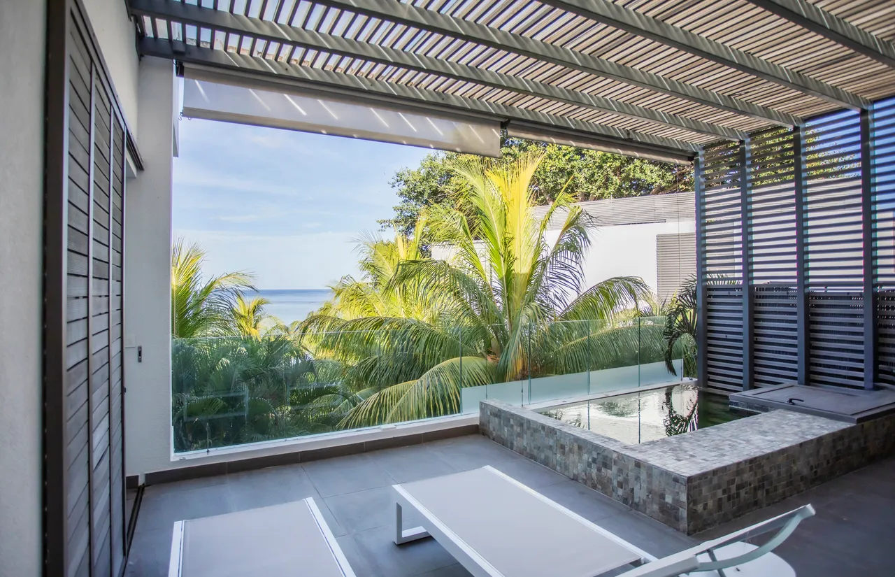 Terrasse avec piscine, offrant une vue sur la mer et la végétation. Chaises longues pour se détendre au soleil.