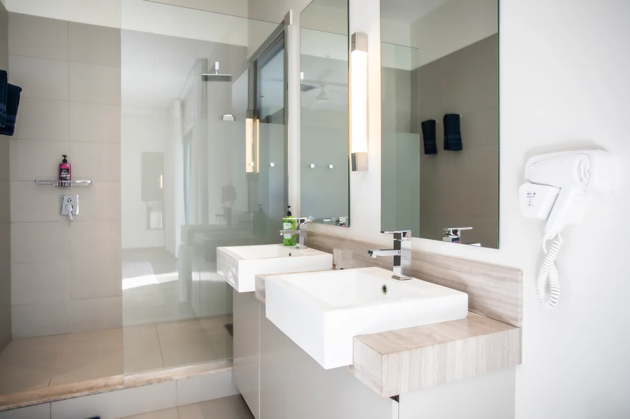 Salle de bain avec douche à l'italienne et deux lavabos. Miroir moderne et rangement intégré.