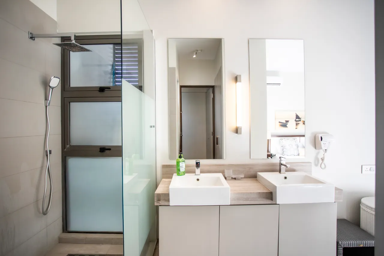 Couleurs claires et matériaux modernes dans la salle de bain. Douche avec paroi en verre et deux lavabos.
