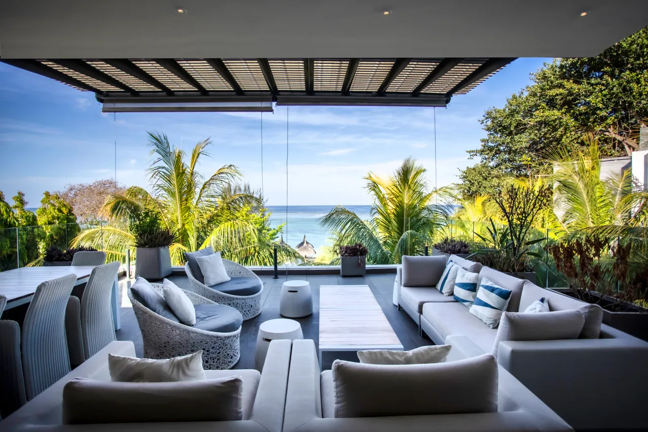 Teintes claires et mobilier en rotin sur la terrasse. Vue sur la mer et la végétation.