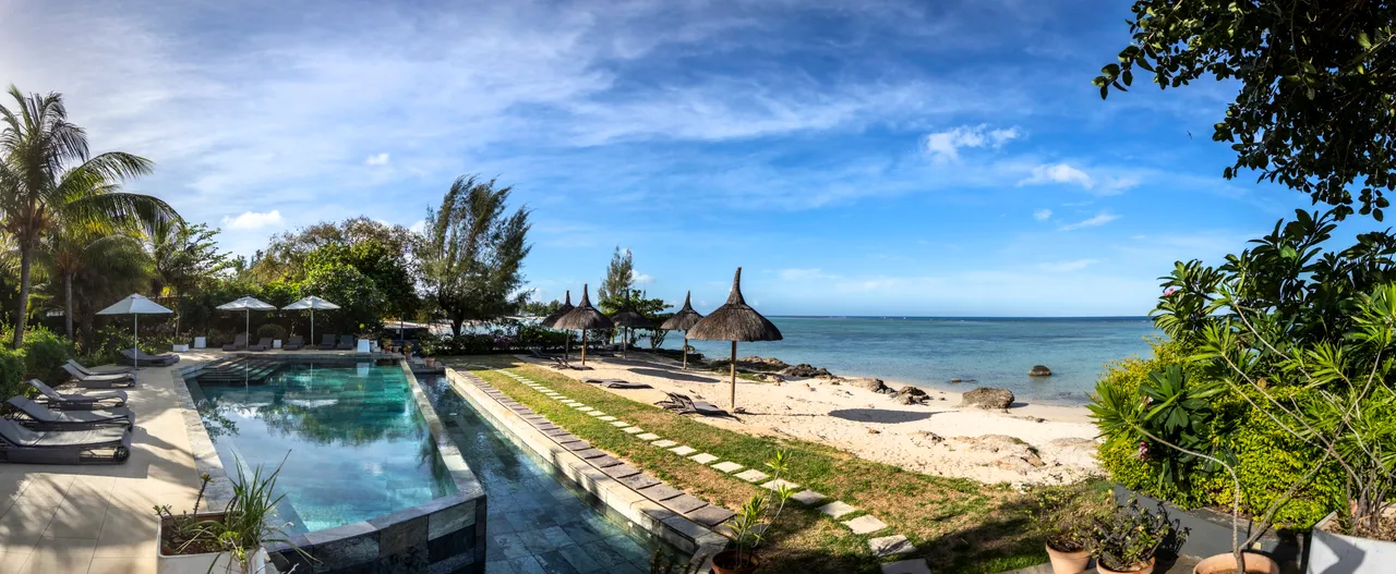Terrasse avec transats et parasols, offrant un accès direct à la plage. Vue sur l'océan.
