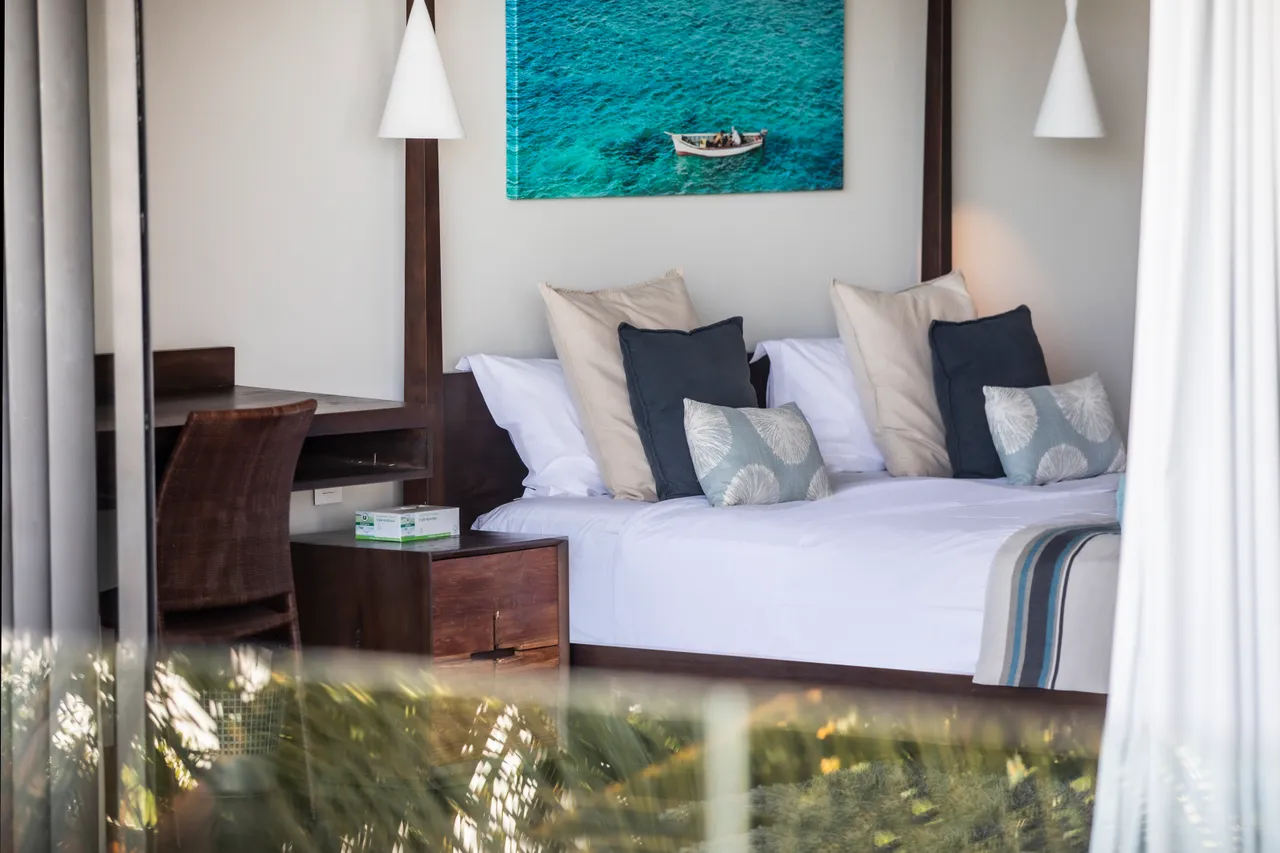Chambre baignée de lumière naturelle avec vue sur la piscine. Bureau en bois et lit confortable.