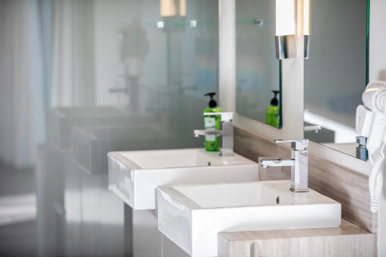 Salle de bain avec deux lavabos et miroir éclairé. Rangement en bois et design épuré.