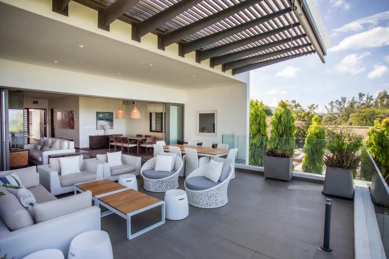 Terrasse en carrelage clair avec mobilier moderne et vue sur la mer. Éclairage naturel crée une atmosphère lumineuse.