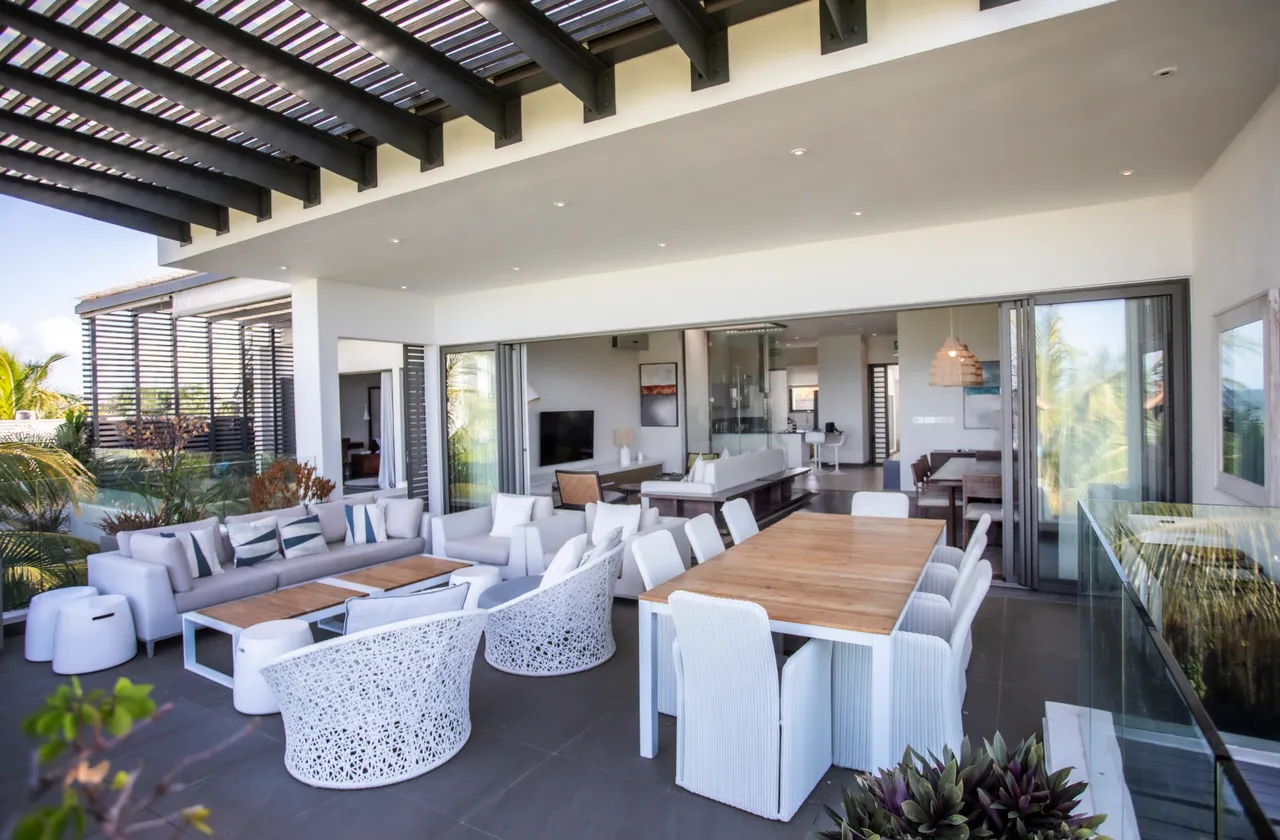 Espace repas avec grandes baies vitrées, ouvrant sur une terrasse ombragée. Mobilier contemporain favorise une atmosphère accueillante.
