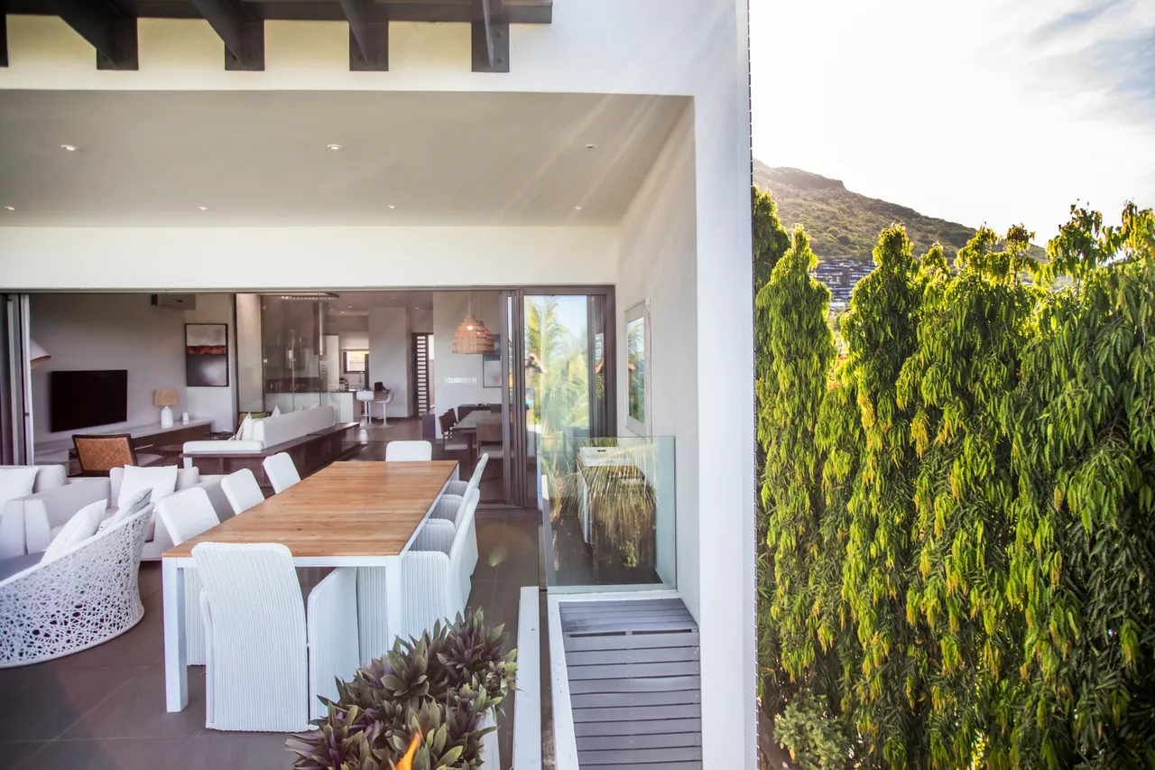Espace repas avec une grande table en bois et chaises blanches. Vue sur la terrasse et l'extérieur.