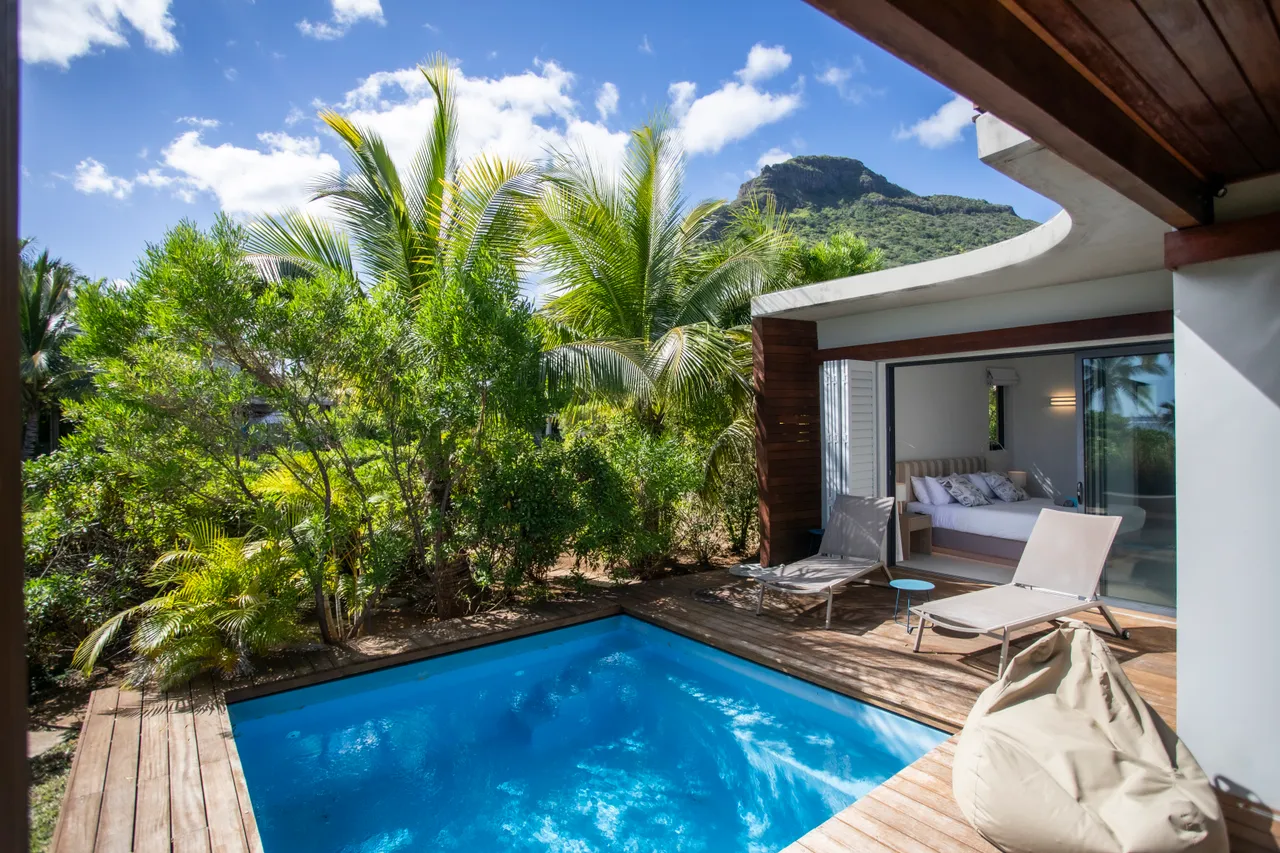 Espace extérieur avec piscine et chaises longues en bois.  

Végétation tropicale créant une atmosphère intime autour de la piscine.  

Coin salon ouvert sur le jardin offrant une vue dégagée.  

Terrasse en bois adjacente à la villa pour profiter du soleil.  

Éléments naturels apportant une touche relaxante à l'environnement.