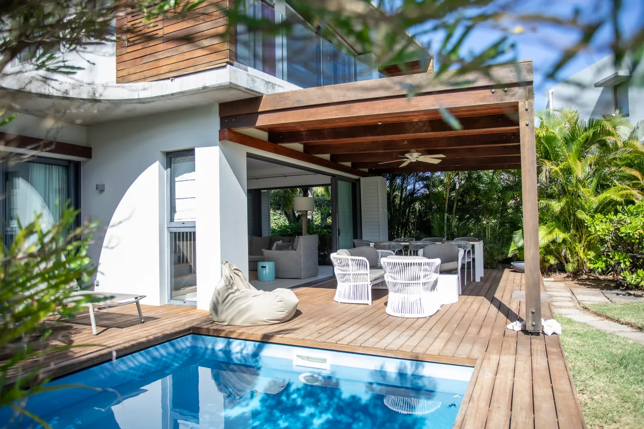 Coin repas en extérieur sous un auvent, face à la piscine.  

Mobilier en rotin sur la terrasse, offrant confort et style.  

Petite piscine intégrée à la terrasse en bois, propice à la détente.  

Végétation tropicale entourant la villa pour une ambiance naturelle.  

Accès à l'intérieur de la villa par de grandes baies vitrées.