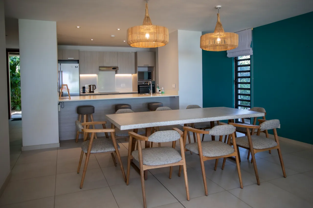 Espace repas avec table en bois et chaises confortables.  

Lumière naturelle provenant des fenêtres créant une ambiance lumineuse.  

Cuisine ouverte attenante, favorisant l'interaction pendant les repas.  

Éléments décoratifs en bois ajoutant une touche chaleureuse à l'espace.  

Mobilier moderne et fonctionnel pour des repas conviviaux.