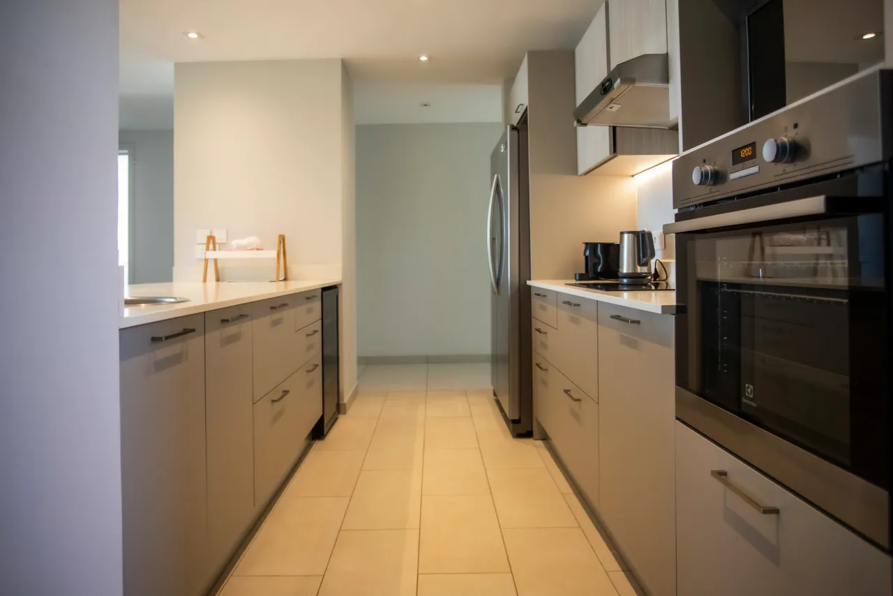 Cuisine complète avec appareils modernes et espace de rangement fonctionnel.  

Plan de travail clair et aménagement optimisé pour la praticité.  

Éclairage intégré fournissant une atmosphère lumineuse et agréable.  

Sol carrelé clair facilitant l'entretien et apportant une touche contemporaine.  

Accès direct à l'espace de vie ouvert, favorisant la circulation.