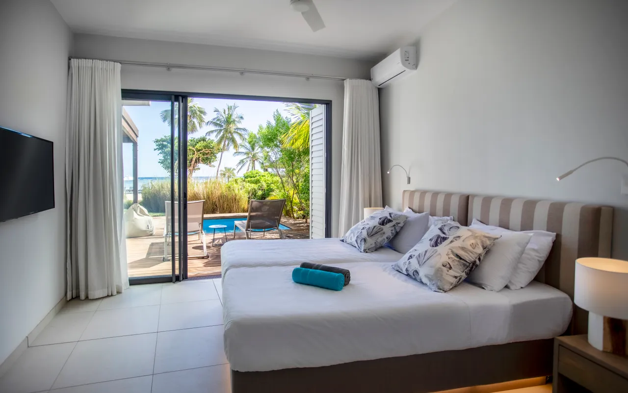 Chambre avec accès direct à une terrasse privée.  

Lits jumeaux disposés pour un espace flexible.  

Fenêtres offrant une vue sur le jardin et la piscine.  

Éclairage doux mettant en valeur la décoration minimaliste.  

Mobilier simple et moderne pour un confort fonctionnel.