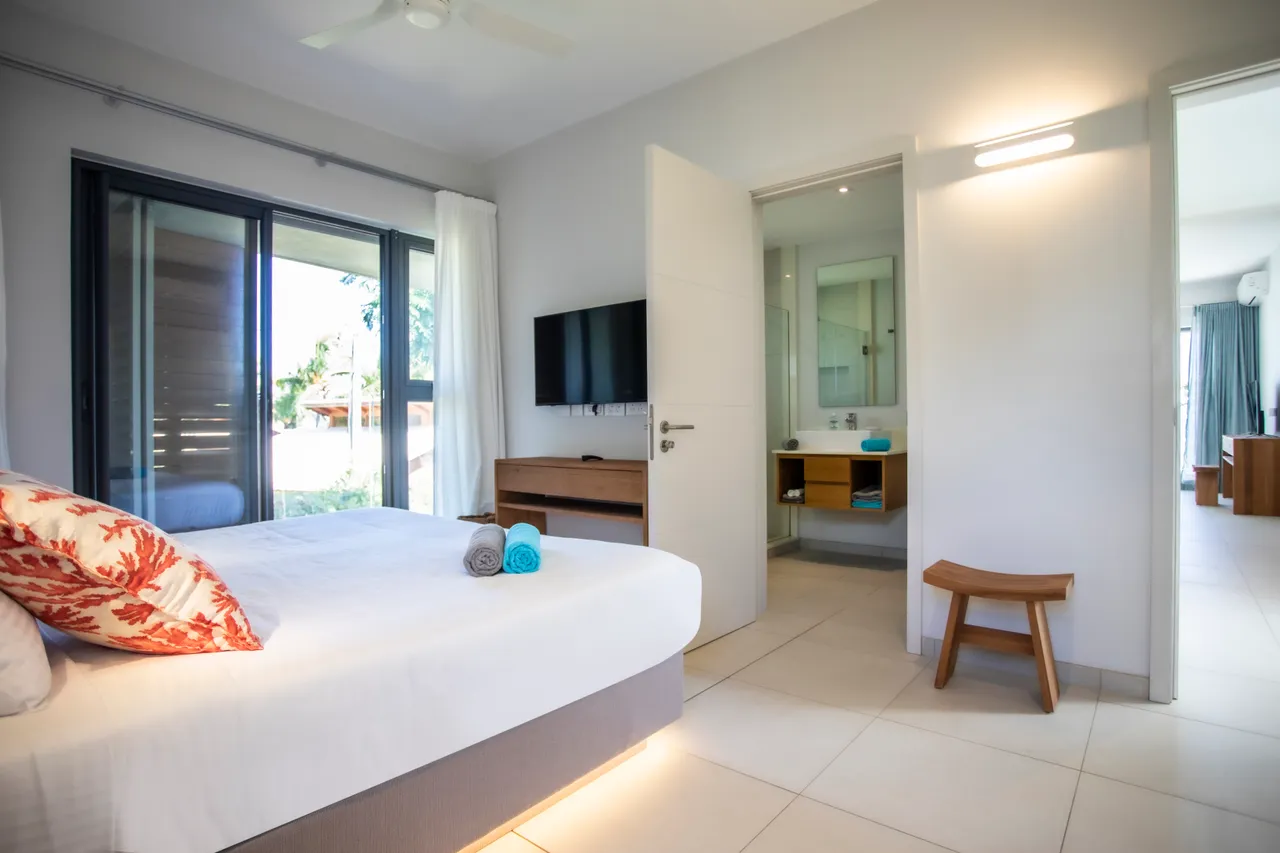 Chambre lumineuse avec accès à une salle de bain attenante.  

Mobilier simple et moderne pour un espace fonctionnel.  

Linge de lit clair et coussins ajoutant une touche de confort.  

Fenêtres offrant une vue sur l'extérieur et favorisant la lumière naturelle.  

Éclairage doux créant une ambiance apaisante dans la pièce.