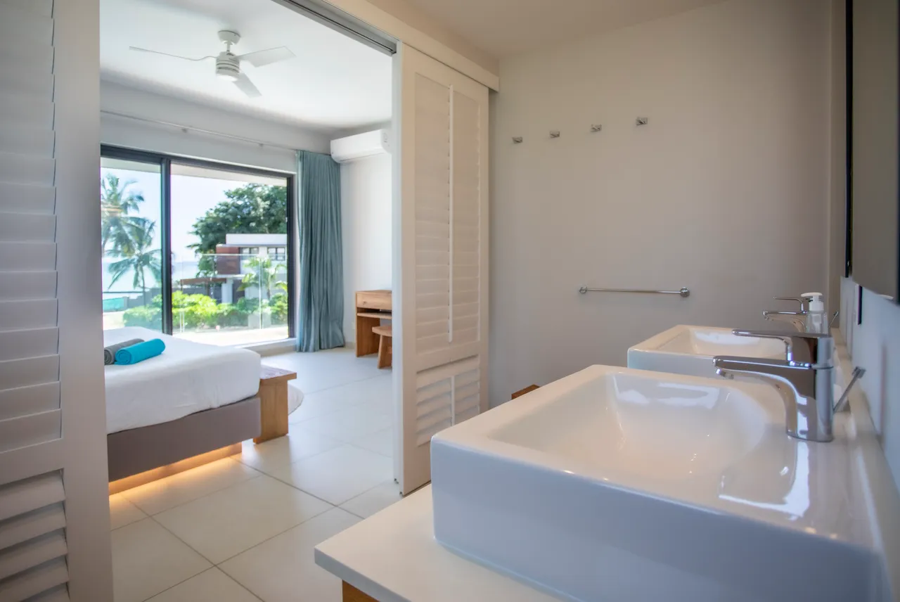Salle de bain équipée de deux vasques et d'un miroir large.  

Douche vitrée offrant une vue sur l'extérieur et luminosité.  

Rangement pratique sous le meuble pour les accessoires de toilette.  

Éléments en bois clair ajoutant une touche de chaleur.  

Ambiance lumineuse grâce à la fenêtre sur l'extérieur.