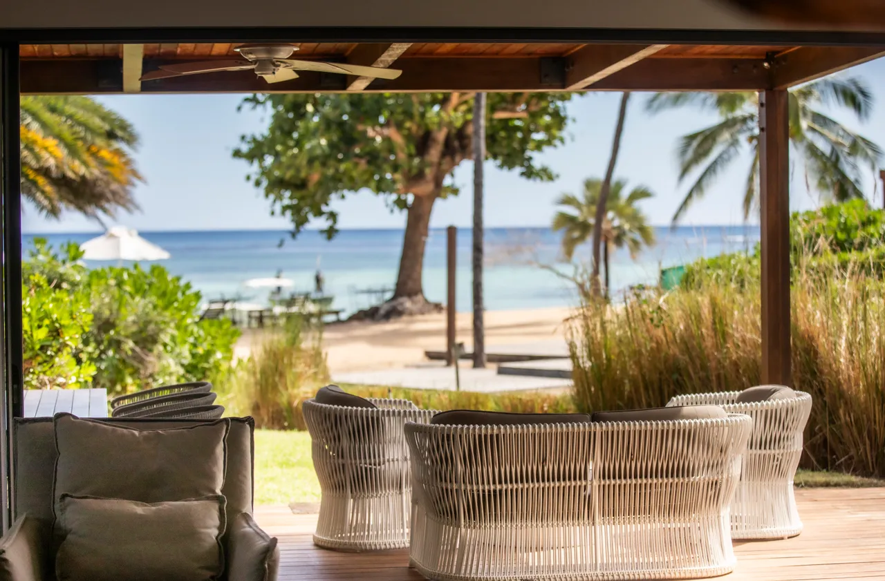 Ouverture sur une vue dégagée sur la plage et la mer.  

Coin salon extérieur avec sièges en rotin pour se détendre.  

Végétation tropicale ajoutant une touche naturelle à l'espace.  

Accès direct au jardin depuis le coin repas extérieur.  

Terrasse spacieuse offrant un cadre agréable pour profiter du plein air.