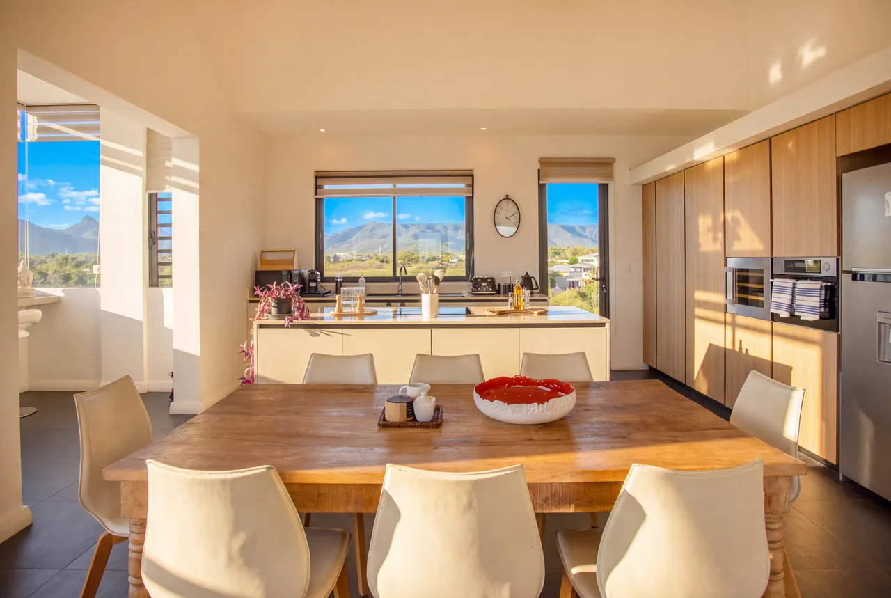 Grande salle à manger avec table en bois et vue sur la mer. Cuisine ouverte avec équipements modernes et rangement.
