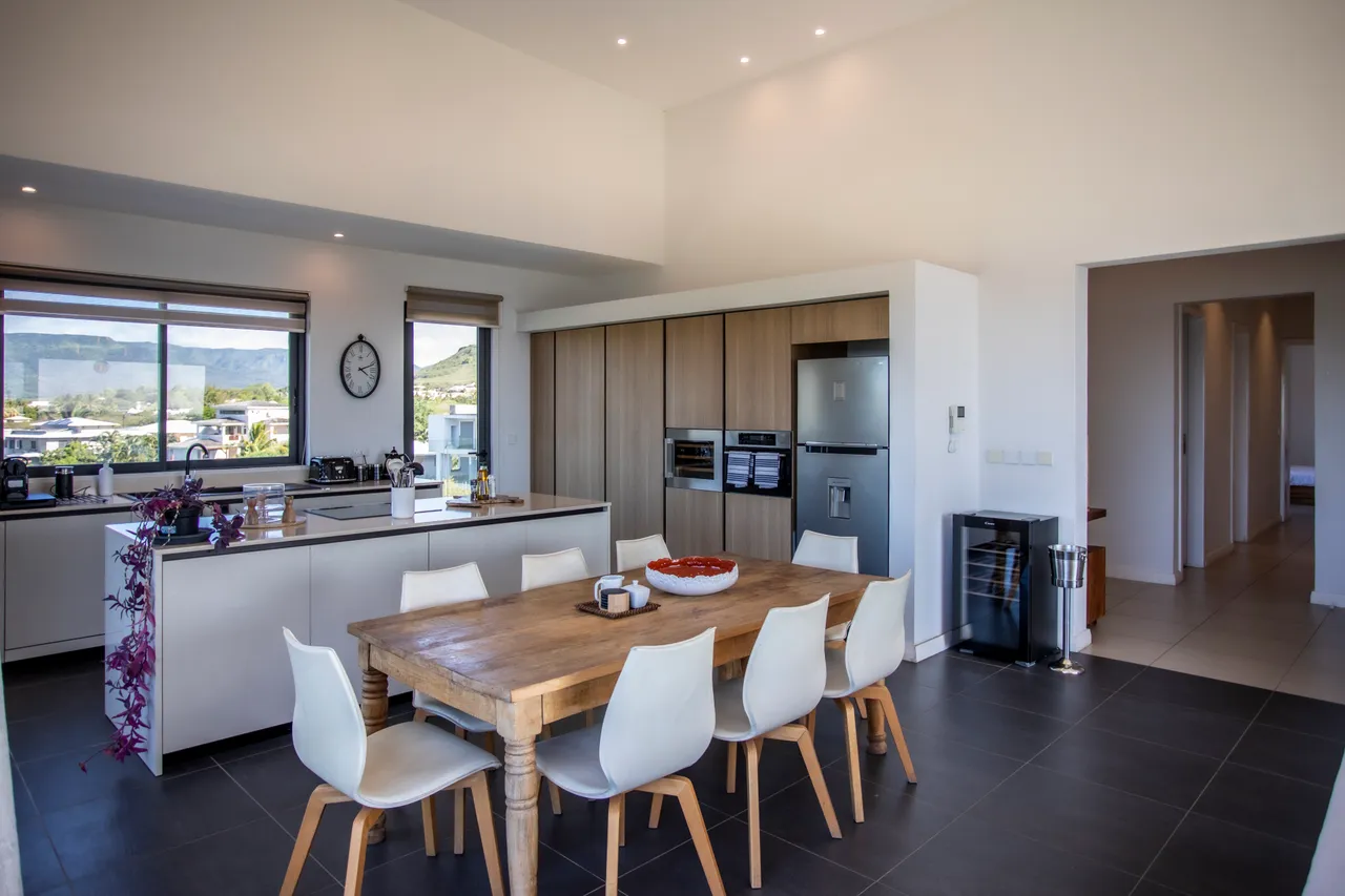 Luminosité naturelle grâce aux grandes fenêtres offrant une vue panoramique. Salle à manger spacieuse avec une table en bois et des chaises contemporaines. Cuisine moderne avec des équipements intégrés et un design épuré. Accès direct à la terrasse pour des repas en extérieur.