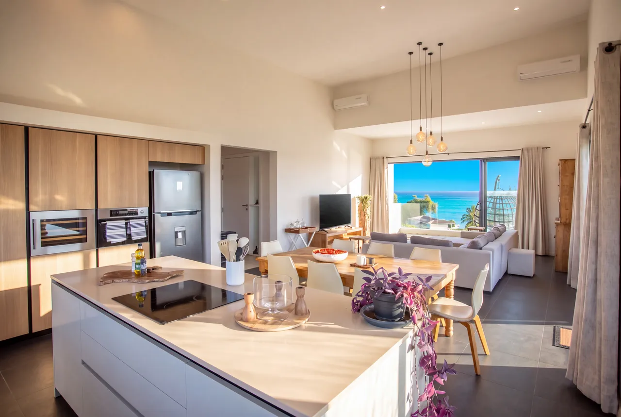 Espace ouvert avec cuisine moderne et grand îlot central. Vue mer depuis le salon lumineux.