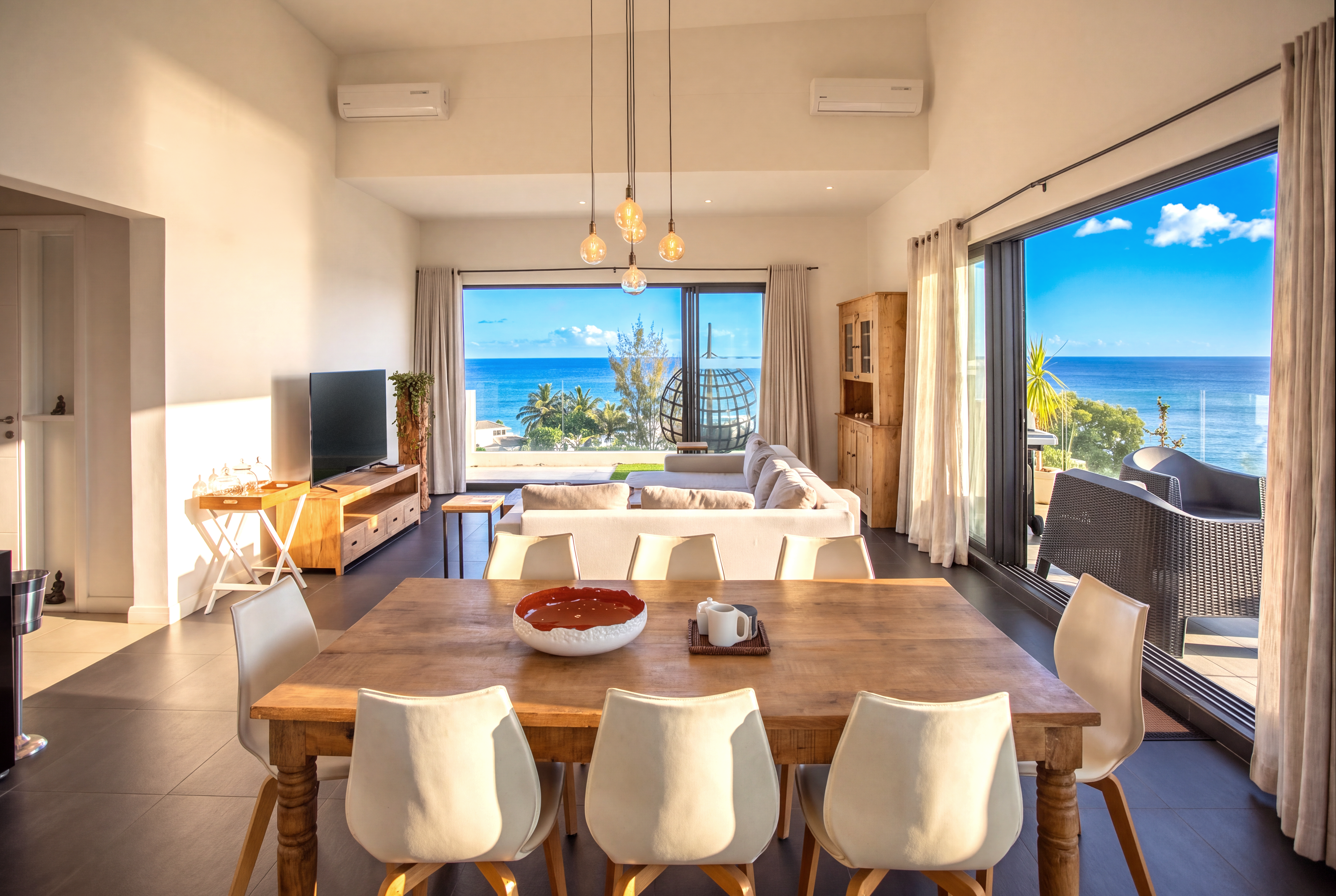 Grandes baies vitrées laissant entrer la lumière et offrant une vue sur la mer. Table en bois avec chaises modernes dans l'espace salle à manger.