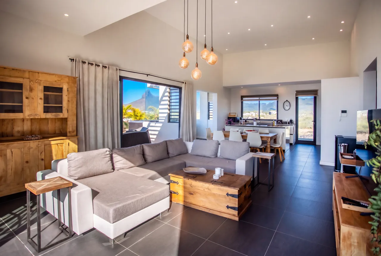 Espace salon avec canapé contemporain et grandes fenêtres sur la mer. Éclairage suspendu ajoutant une touche moderne à l'ensemble.