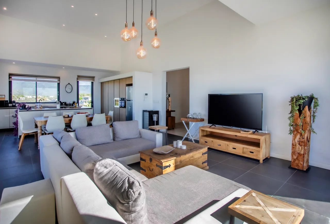 Espace galerie baigné de lumière naturelle avec vue sur la mer. Canapé contemporain et télévision dans le salon. Mobilier en bois ajoutant une touche chaleureuse. Cuisine ouverte à proximité, facilitant la convivialité.