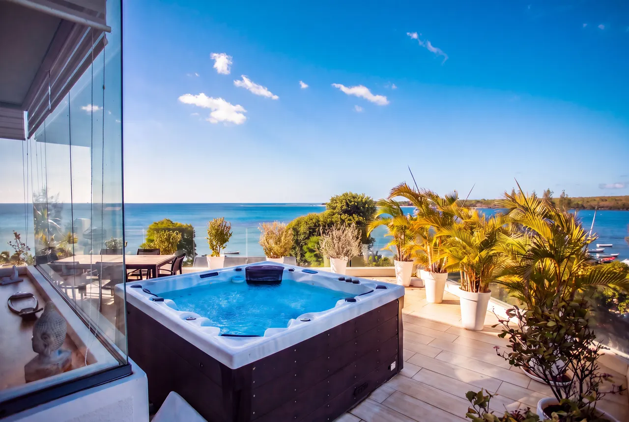 Jacuzzi sur la terrasse avec vue directe sur la mer. Espace extérieur entouré de végétation.