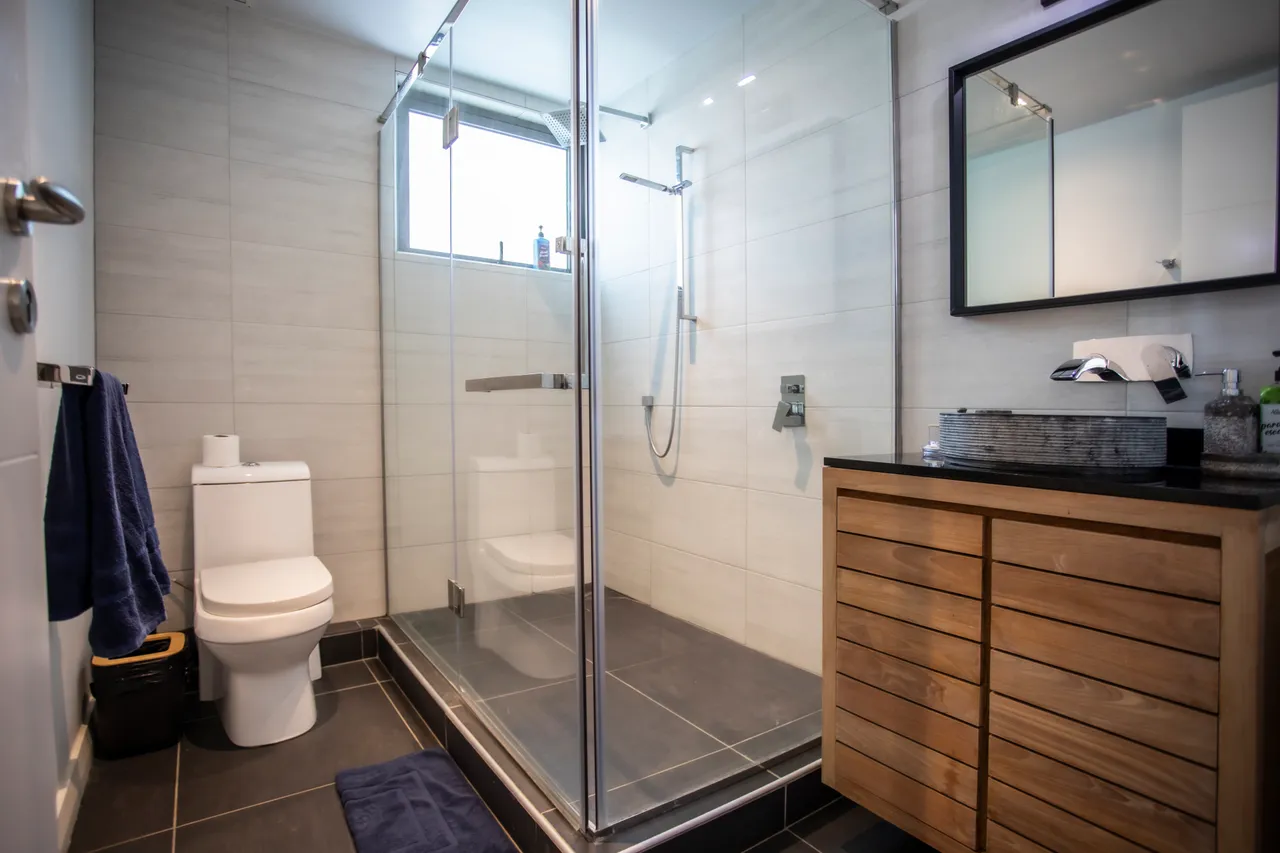 Salle de bain moderne avec douche italienne et meubles en bois. Éclairage naturel grâce à une fenêtre.