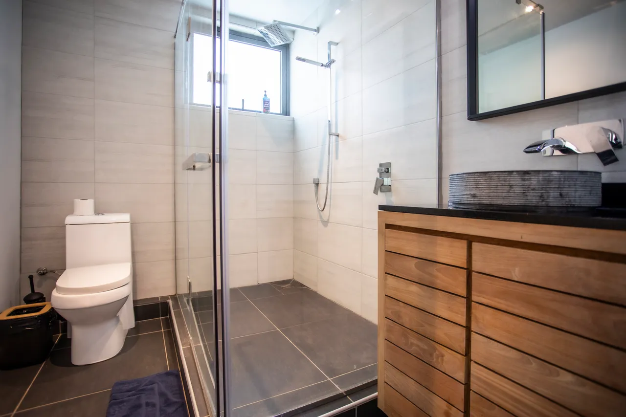 Salle de bain équipée d'une douche italienne et de rangements en bois. Éclairage naturel provenant d'une fenêtre.