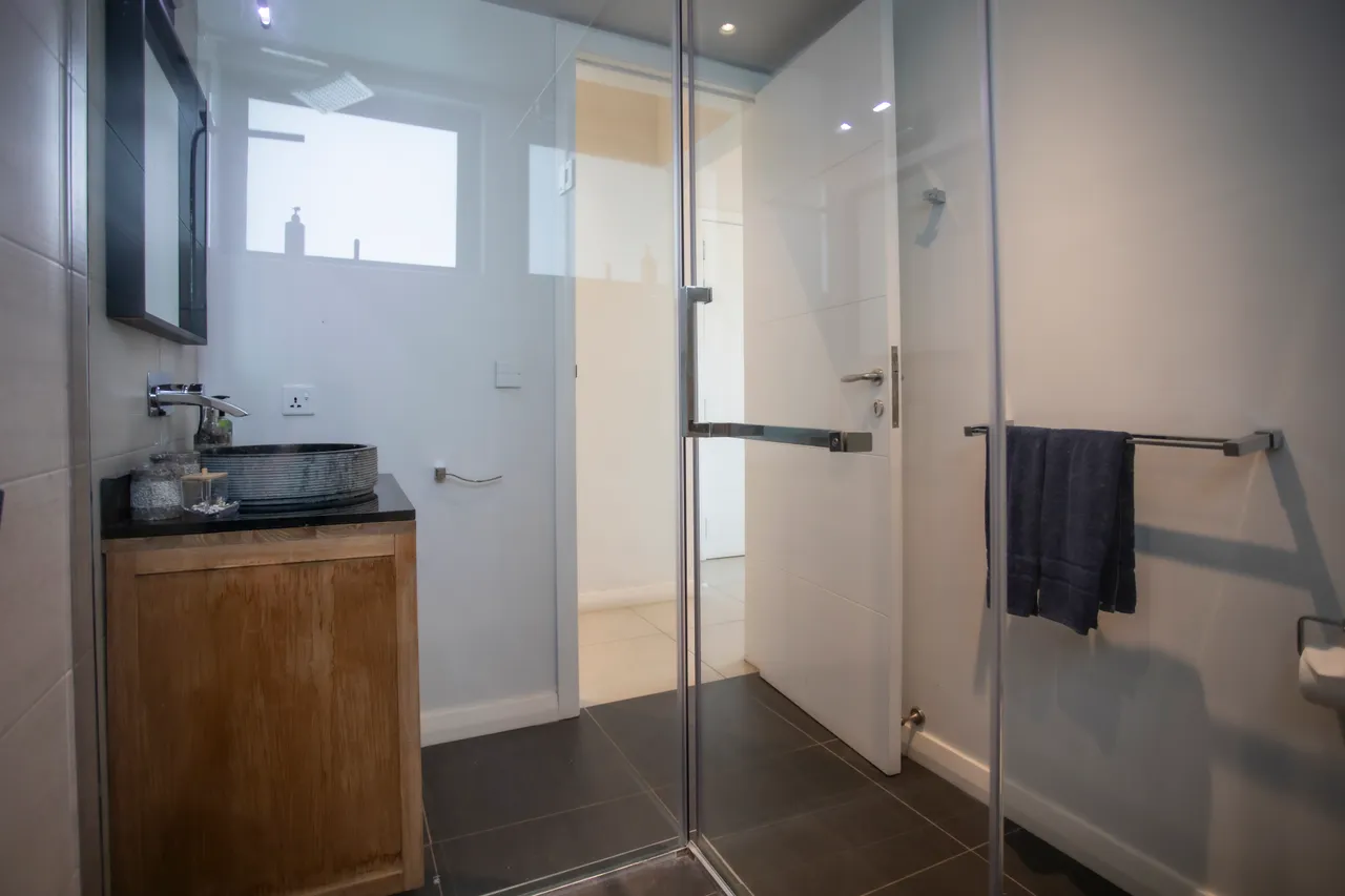 Salle de bain moderne avec douche en verre et meuble en bois clair. Espace lumineux grâce à une fenêtre.