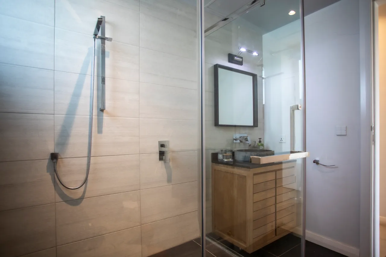 Salle de bain spacieuse avec douche à l'italienne et rangement en bois. Éclairage naturel par une fenêtre.