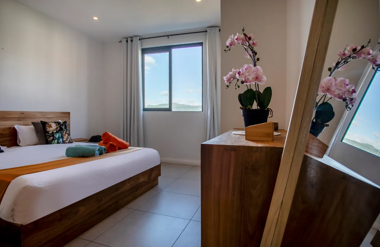 Chambre avec un lit double et rangement en bois. Fenêtre offrant une vue dégagée sur l'extérieur.