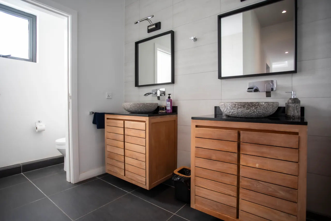 Salle de bain avec doubles vasques en pierre et meubles en bois. Éclairage naturel par une fenêtre.