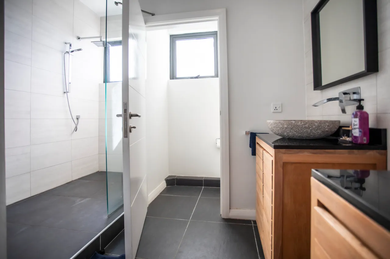 Mur en carrelage clair, salle de bain avec douche en verre et meuble en bois. Éclairage naturel par une fenêtre.
