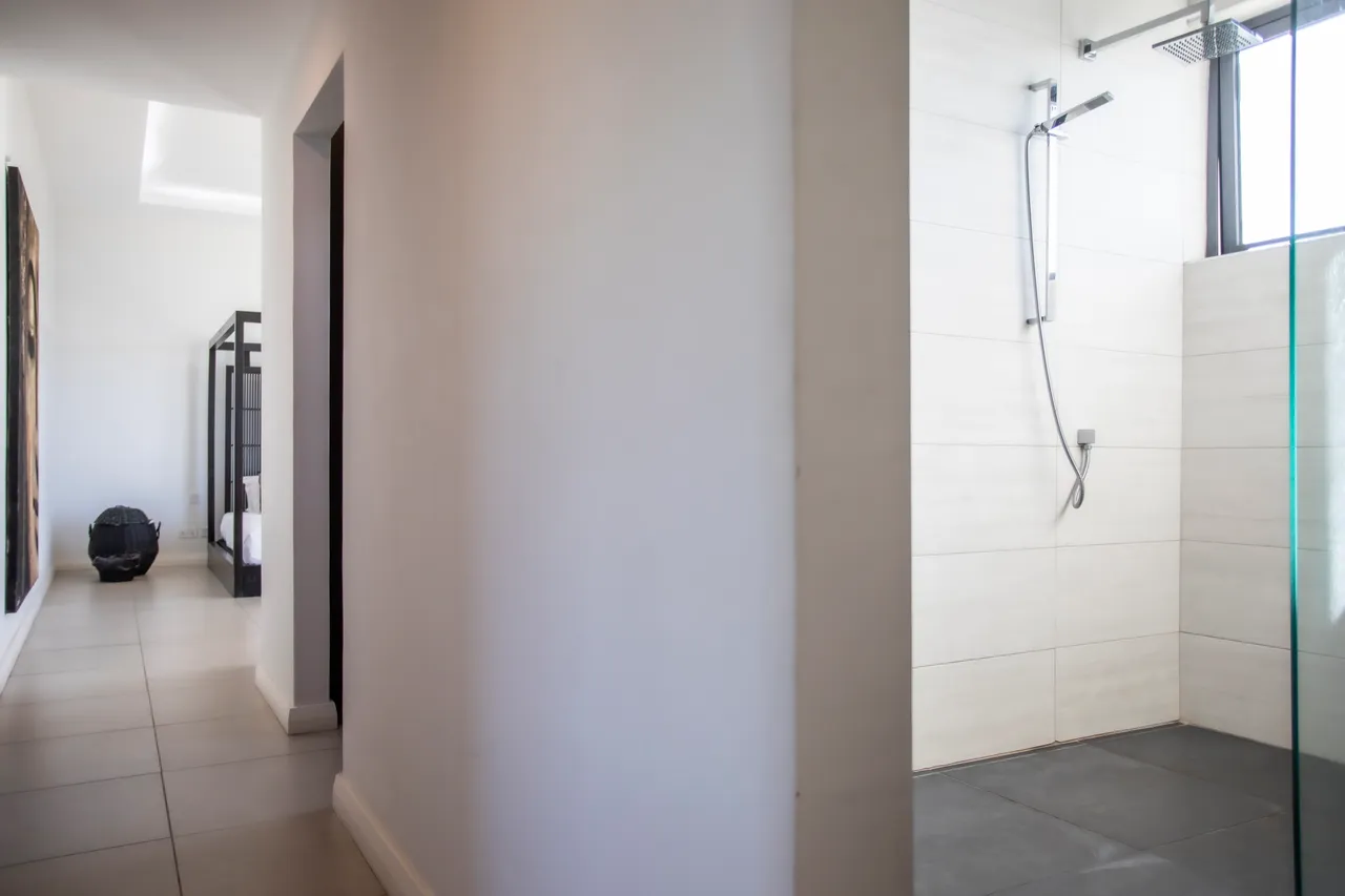 Galerie avec carreaux clairs et douche en verre. Accès à des espaces lumineux.