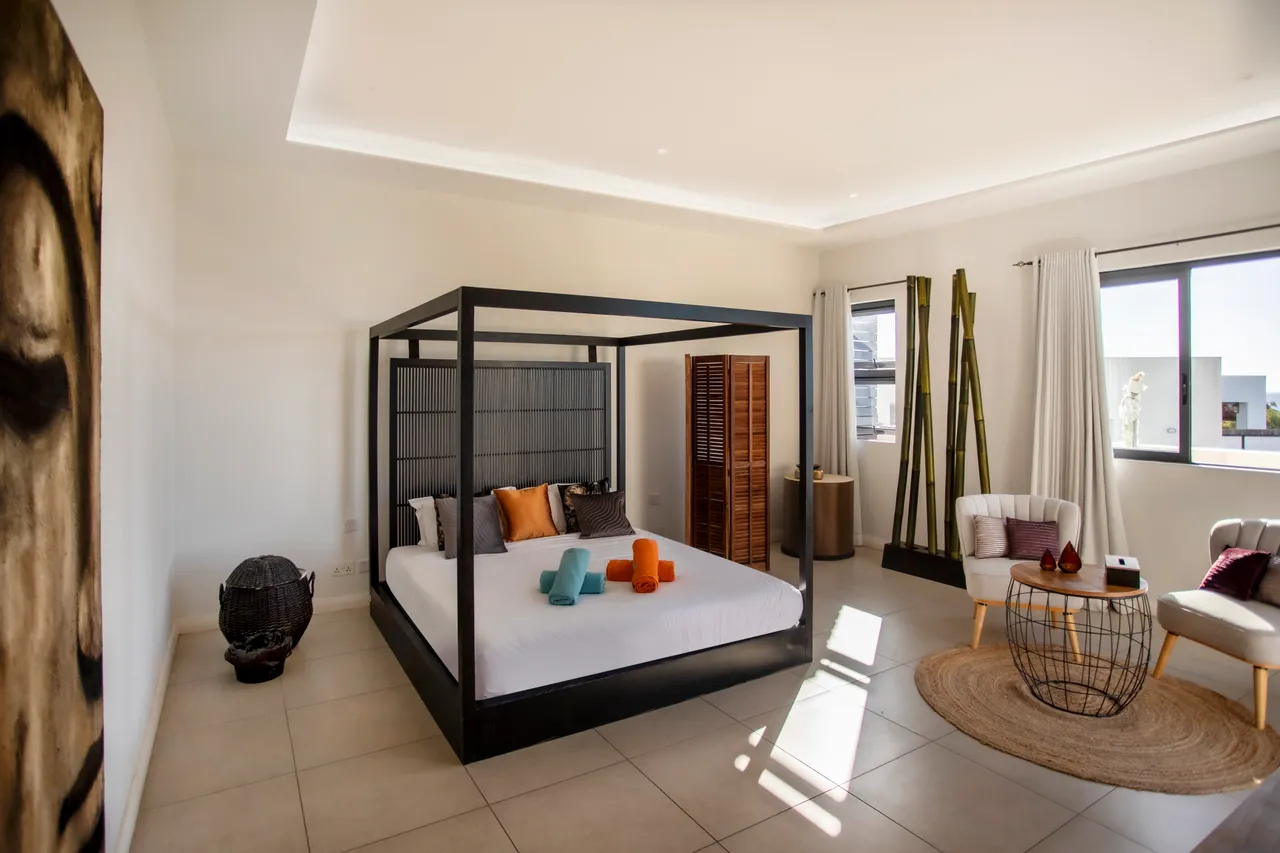 Chambre avec un lit à baldaquin noir et sièges contemporains. Éclairage naturel abondant par fenêtres.