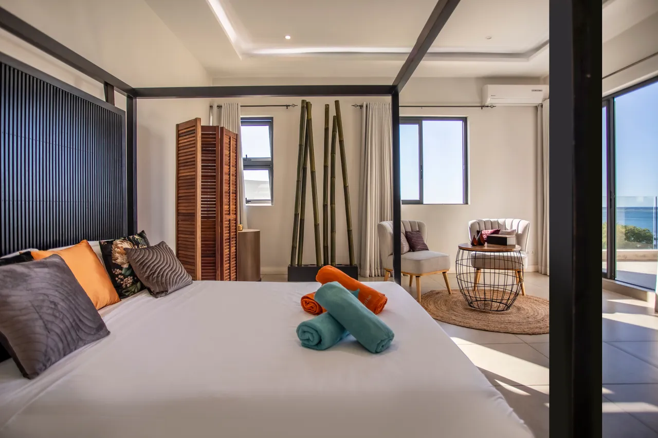 Chambre avec un lit à baldaquin et coin salon. Grandes fenêtres offrant une vue sur la mer.