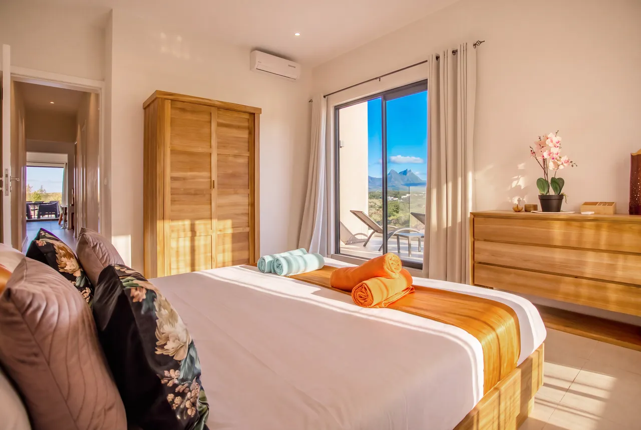 Tons chaleureux et mobilier en bois. Chambre avec lit double et accès à un balcon.