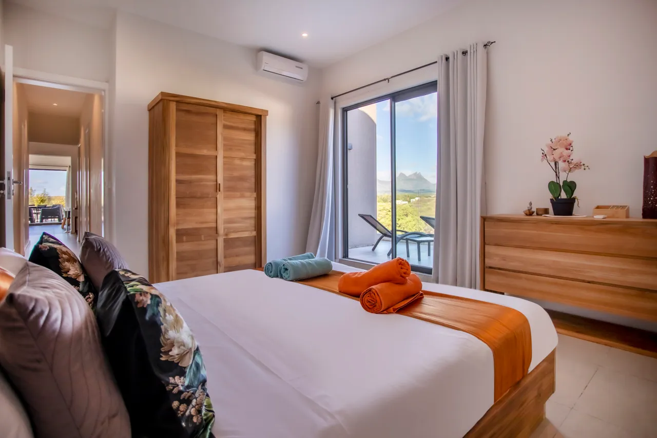 Chambre avec un lit en bois et un rangement intégré. Accès à un balcon.