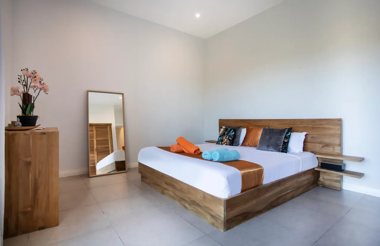 Chambre avec lit en bois et décoration colorée. Miroir sur pied et éclairage naturel.