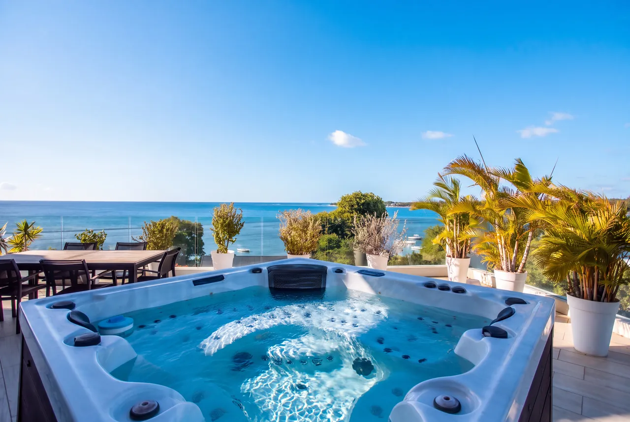 Jacuzzi en extérieur avec vue dégagée sur la mer. Mobilier de jardin en bois.