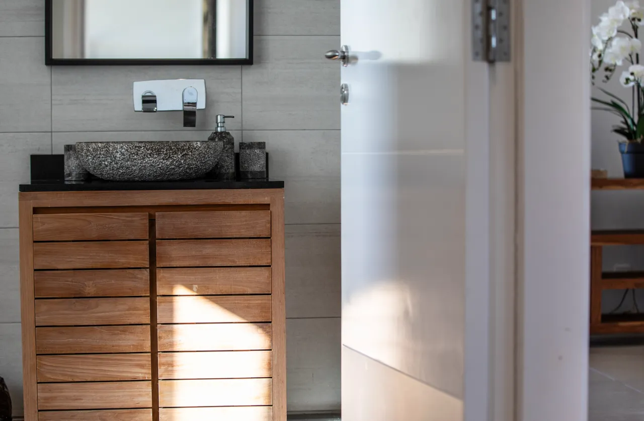 Meuble de salle de bain en bois avec tiroirs et vasque en pierre. Éclairage naturel accentué par une fenêtre.