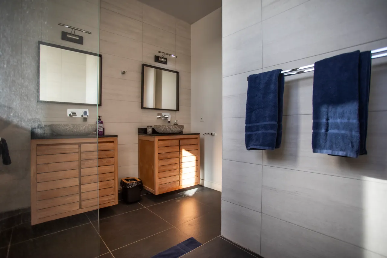 Salle de bain lumineuse équipée de deux lavabos et de miroirs. Mobilier en bois bien agencé.