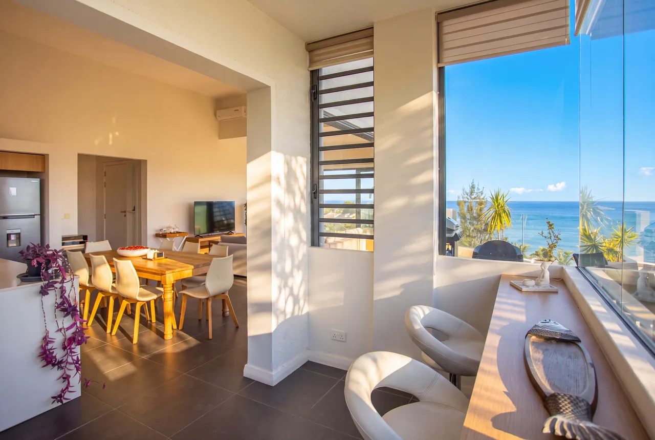 Galerie avec coin repas et grandes fenêtres offrant une vue sur l'extérieur. Mobilier moderne et lumineux.