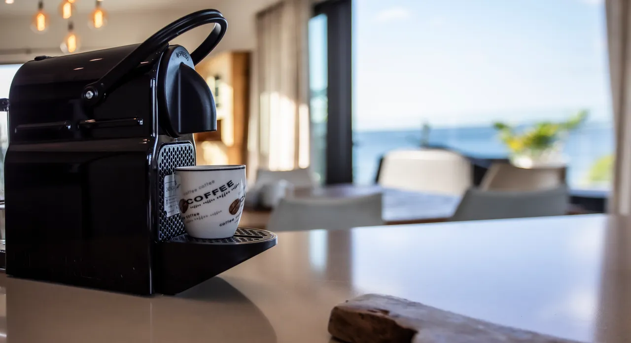 Machine à café moderne sur un plan de travail en marbre. Vue sur la mer à l'arrière.